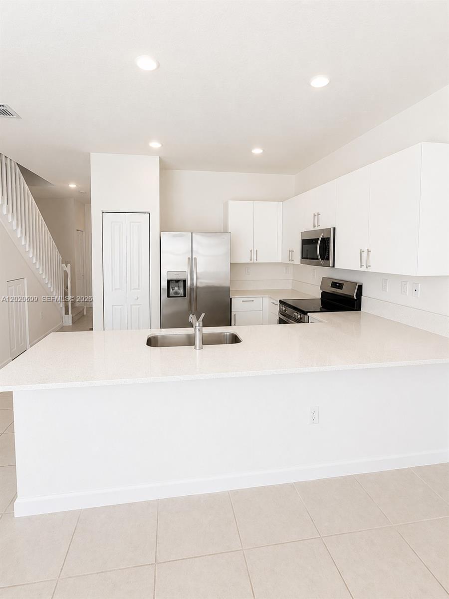 A modern kitchen features white cabinets, stainless steel appliances, and a quartz-topped peninsula island — 2840 SE 26th Ter, Homestead FL 33035, HOMESTEAD, FL