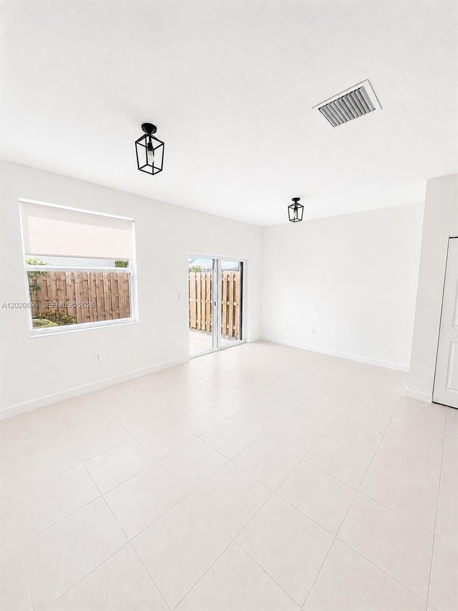 A bright, empty room features white tile flooring, two pendant lights, and a sliding glass door — 2840 SE 26th Ter, Homestead FL 33035, HOMESTEAD, FL