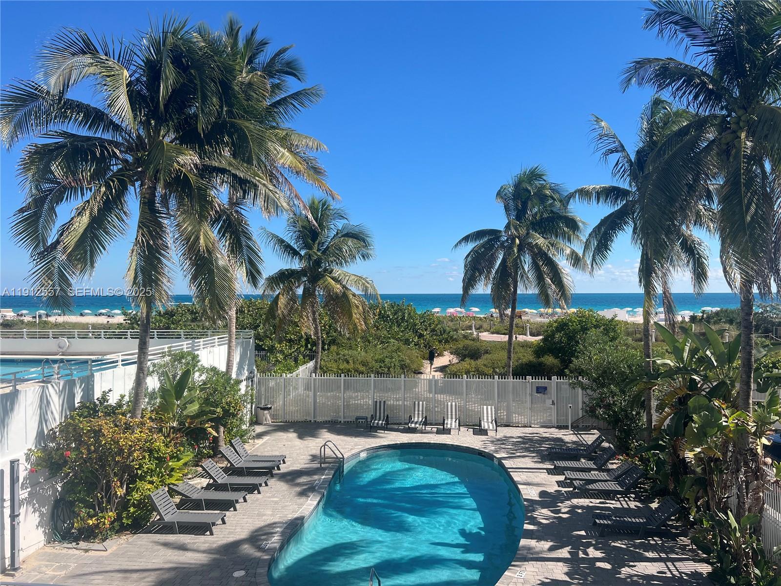 An outdoor swimming pool is surrounded by lounge chairs, palm trees, and a beach view — 335 Ocean Dr # 328, Miami Beach FL 33139, MIAMI BEACH, FL