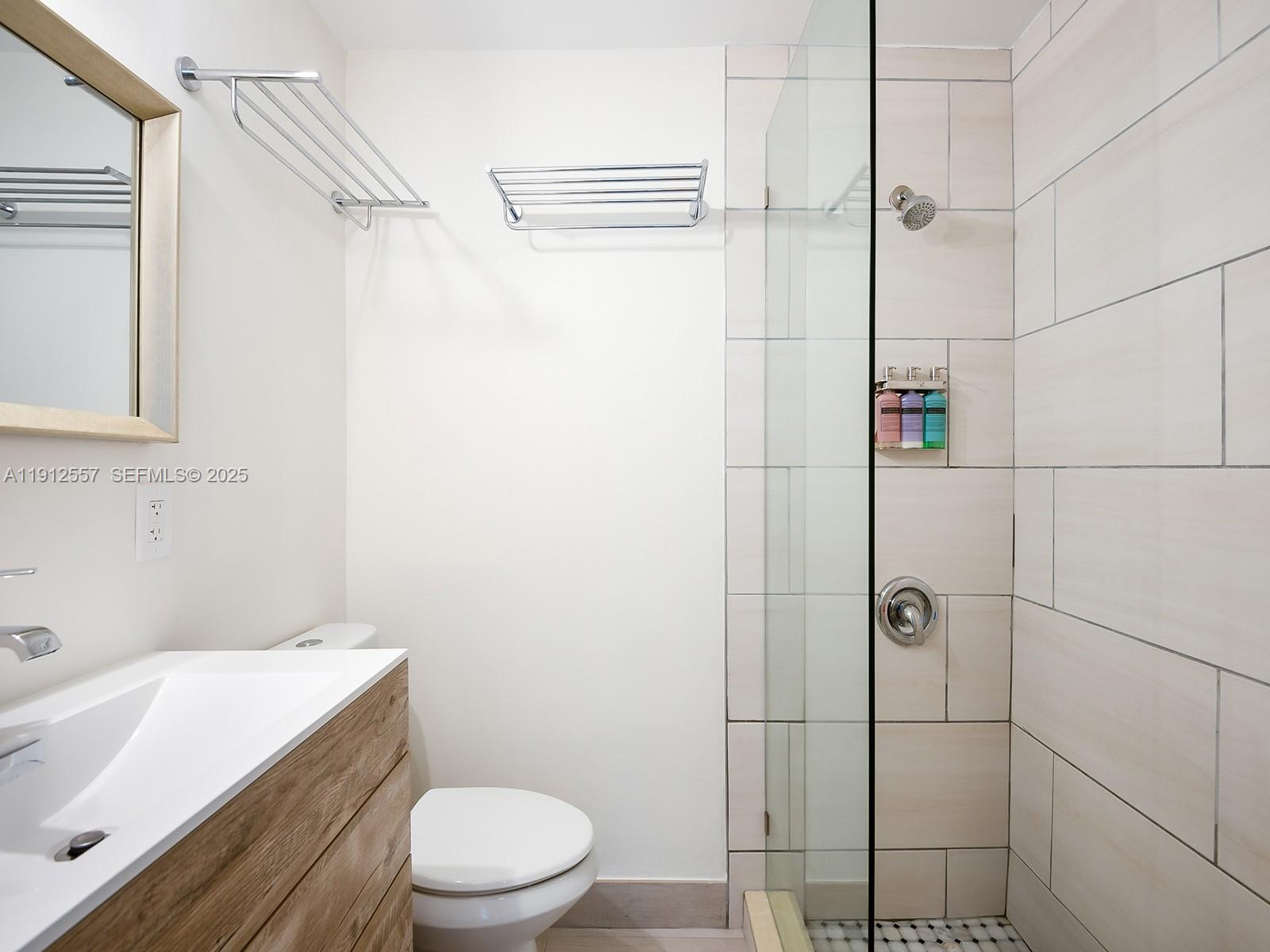 A modern bathroom features a wood-grain vanity, a glass-enclosed shower, and wall-mounted towel racks — 335 Ocean Dr # 328, Miami Beach FL 33139, MIAMI BEACH, FL