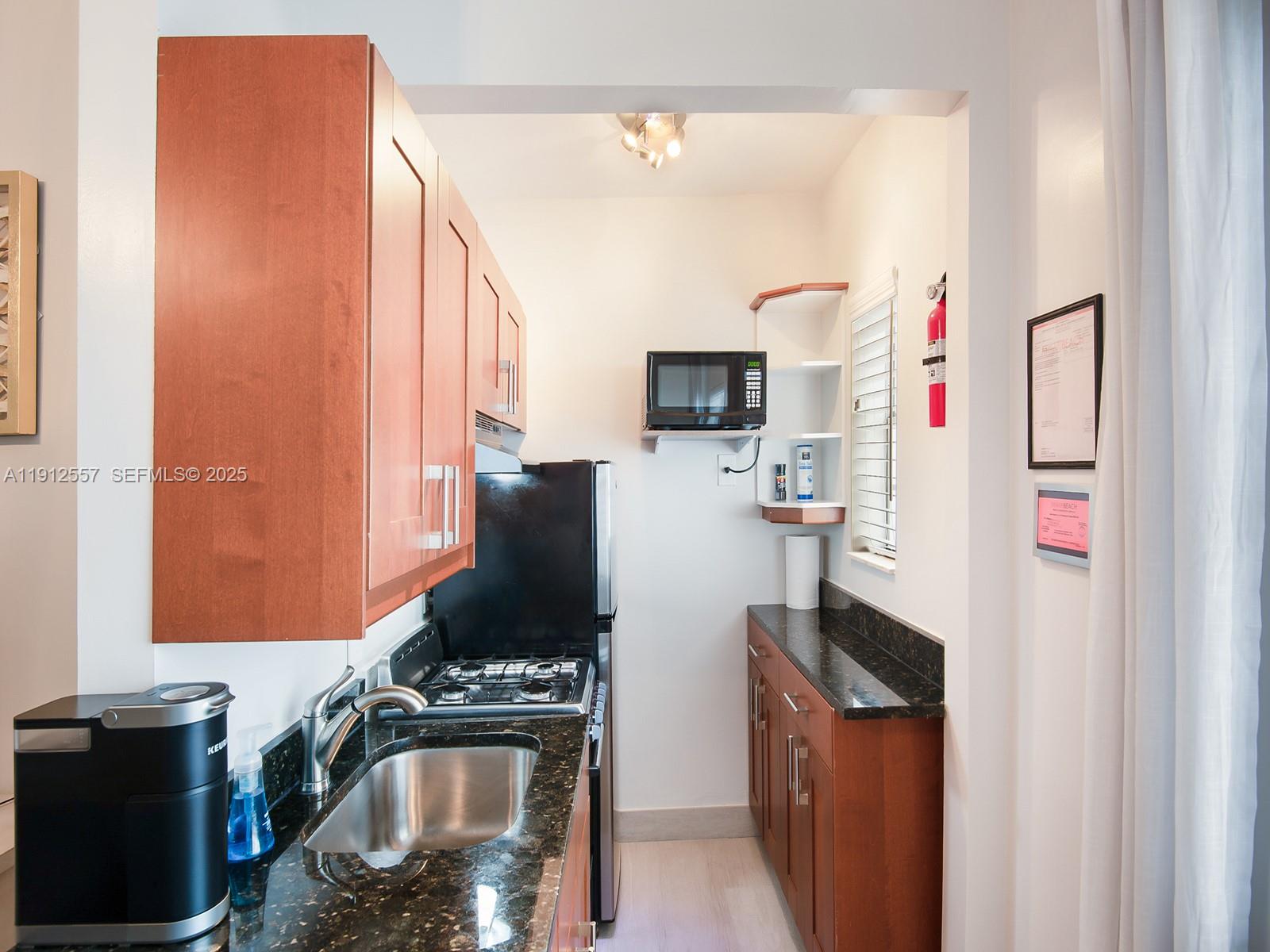 A galley kitchen features wood cabinets, dark granite countertops, a stainless steel sink, and appliances — 335 Ocean Dr # 328, Miami Beach FL 33139, MIAMI BEACH, FL