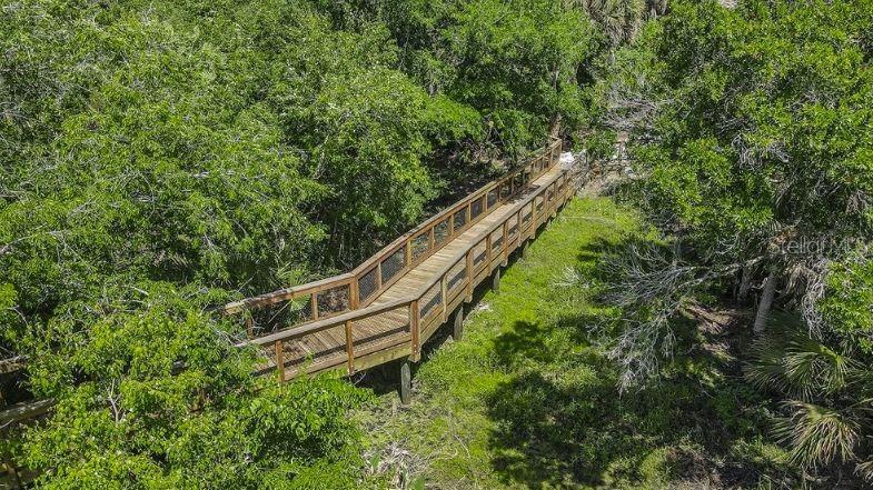 An elevated wooden boardwalk winds through a dense, green forest — 7808 CENTAURUS WAY, SARASOTA, FL