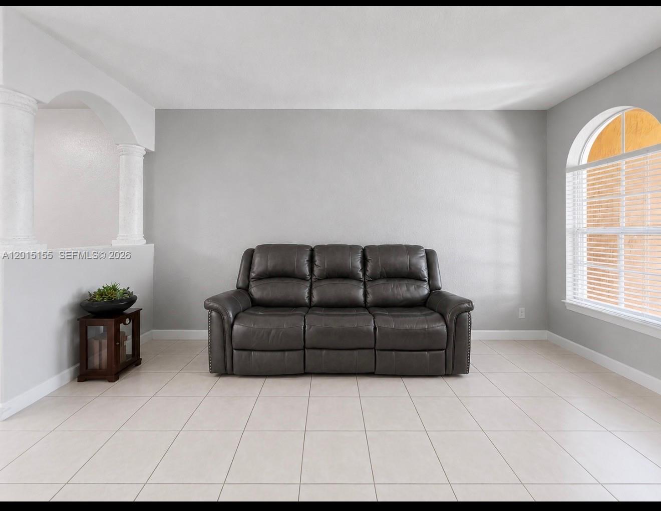 A gray leather reclining sofa sits against a wall in a room with tile flooring — 1441 SE 24th Rd, Homestead FL 33035, HOMESTEAD, FL