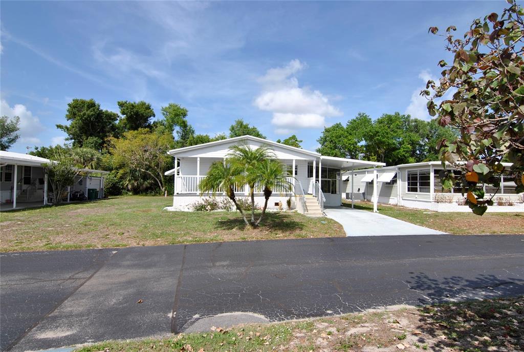 A white manufactured home with a front porch, palm trees, and a paved driveway — 24437 HARBORVIEW ROAD UNIT 106, PUNTA GORDA, FL