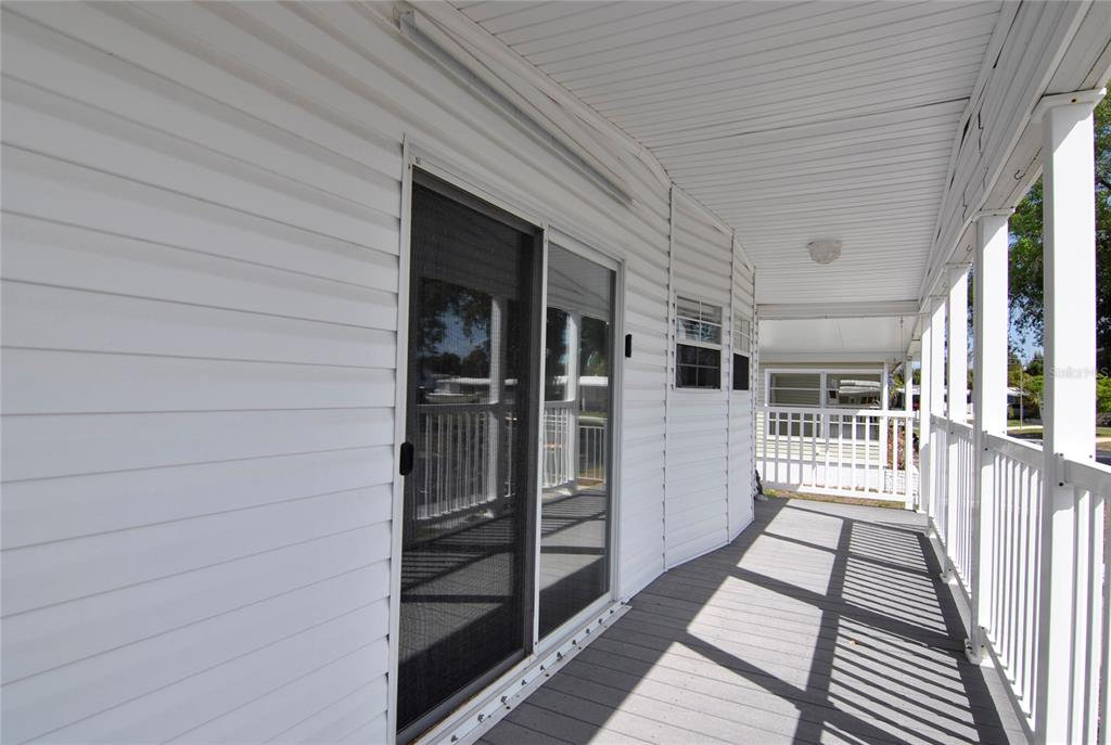 A covered porch with white siding, a sliding glass door, and a wooden deck — 24437 HARBORVIEW ROAD UNIT 106, PUNTA GORDA, FL