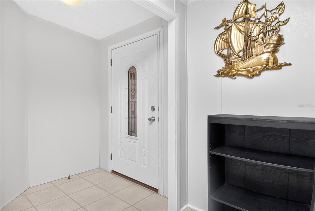 An entryway features a white door, tiled floor, and a gold ship wall decoration — 24437 HARBORVIEW ROAD UNIT 106, PUNTA GORDA, FL