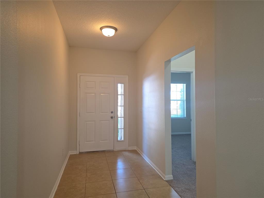 An entryway with tiled flooring, a white front door with sidelight, and a carpeted room beyond — 311 RAMBLING CIRCLE, APOPKA, FL
