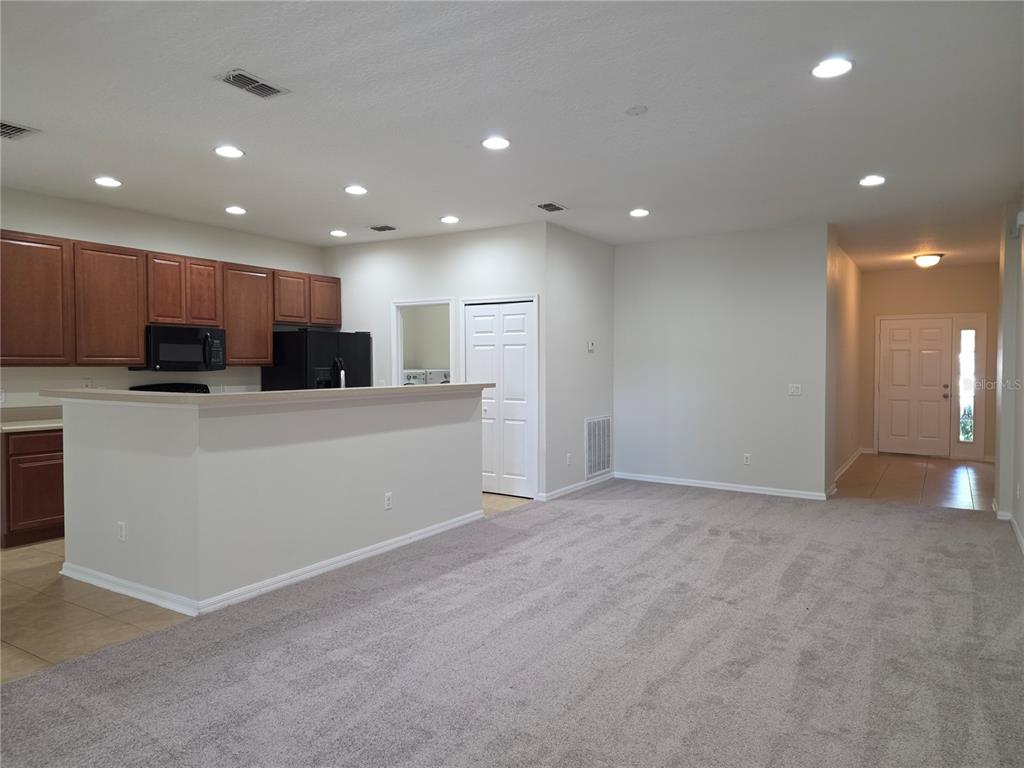 An open-concept kitchen with wood cabinets and a breakfast bar overlooks a carpeted living area — 311 RAMBLING CIRCLE, APOPKA, FL