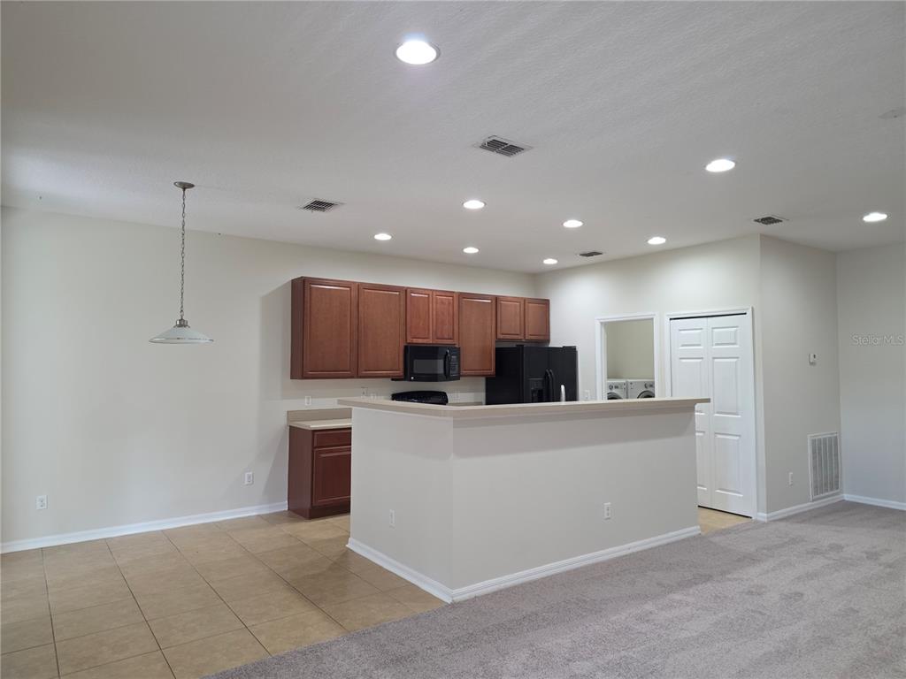 A kitchen with wooden cabinets and a breakfast bar overlooks a carpeted living area — 311 RAMBLING CIRCLE, APOPKA, FL
