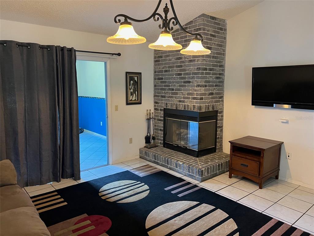 A living room features a gray brick corner fireplace, tile flooring, and a patterned area rug — 330 BONNIE LANE, ORANGE CITY, FL
