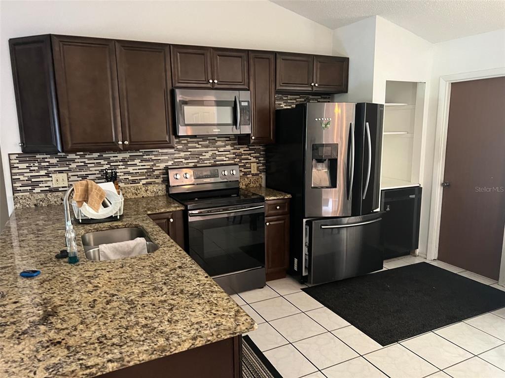 A kitchen features dark wood cabinets, granite countertops, stainless steel appliances, and a tiled floor — 330 BONNIE LANE, ORANGE CITY, FL