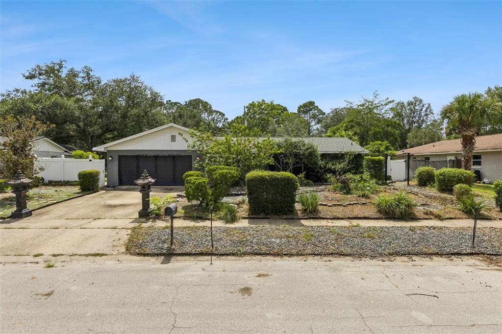 A single-story house with a two-car garage, gravel front yard, and mature landscaping — 129 MARGO LANE, LONGWOOD, FL