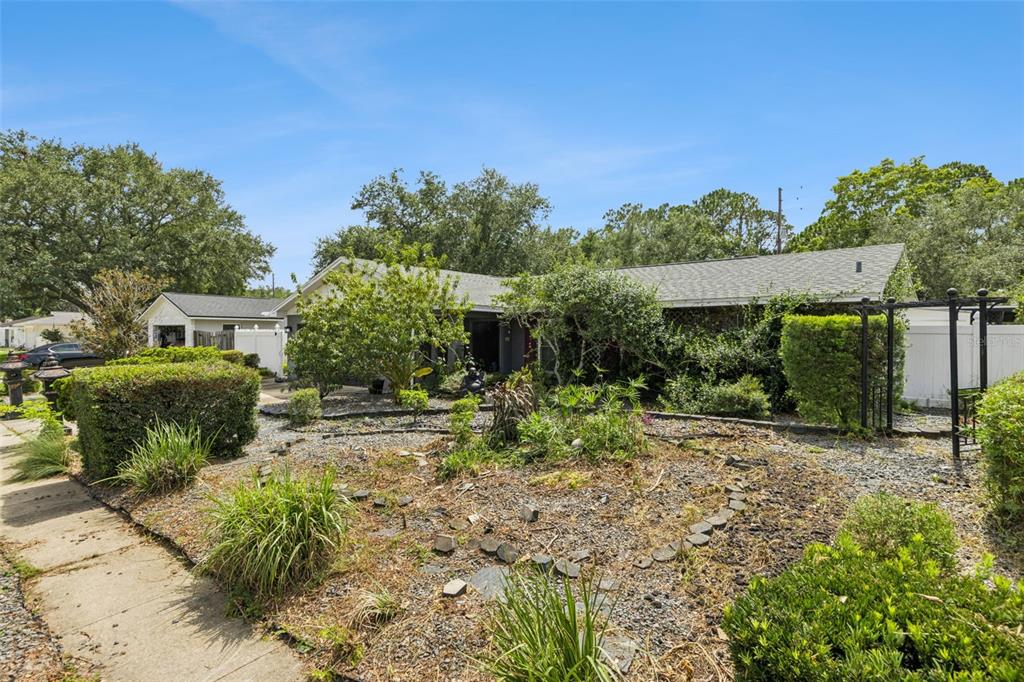 A single-story house with a gravel front yard, overgrown landscaping, and a metal trellis — 129 MARGO LANE, LONGWOOD, FL