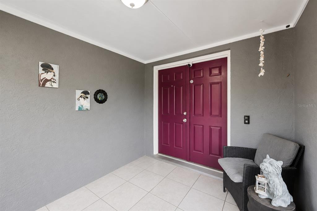 A covered entryway features a dark red double door, gray walls, and tiled flooring — 129 MARGO LANE, LONGWOOD, FL