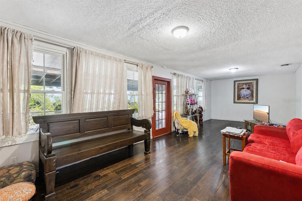 A living room features dark wood flooring, a red sofa, a wooden bench, and white walls — 129 MARGO LANE, LONGWOOD, FL