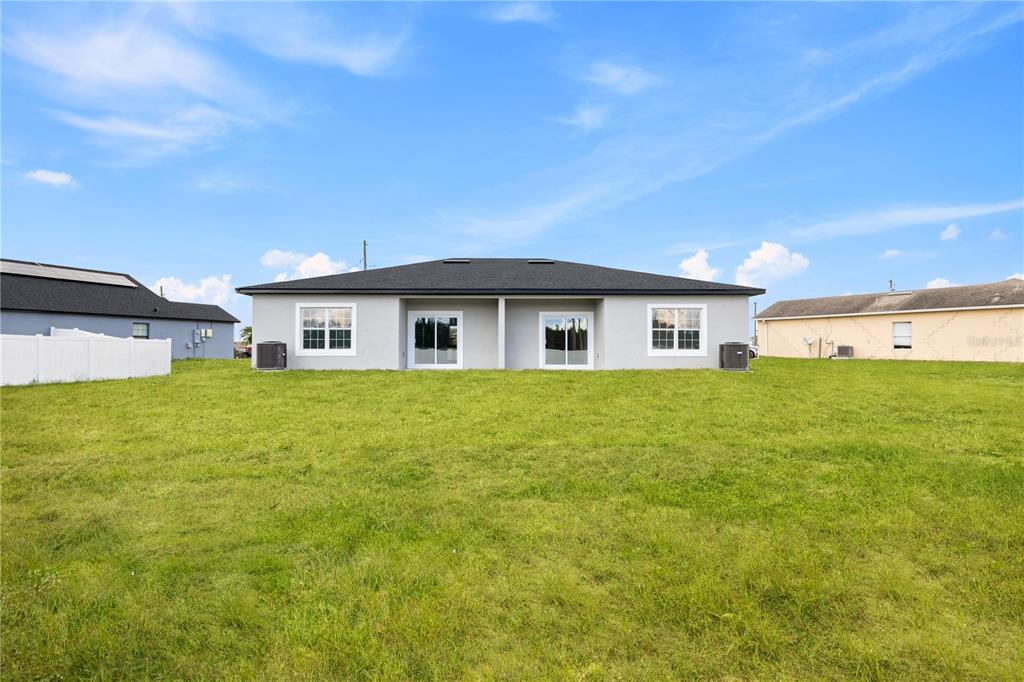 The rear exterior of a single-story duplex features a gray facade, two sliding glass doors, and windows — 476-474 COLUMBIA COURT, POINCIANA, FL