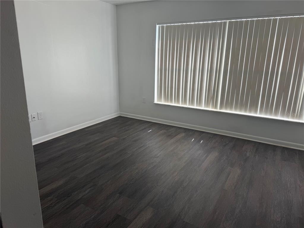 An empty room with white walls and dark wood-look flooring features a closed door — 2262 MENOMONEE COURT, ORLANDO, FL