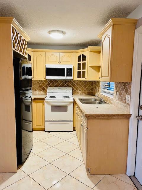 A kitchen features light wood cabinets, a black refrigerator, white appliances, and beige tile flooring — 4491 NW 1st Terrace, Deerfield Beach FL 33064, DEERFIELD BEACH, FL