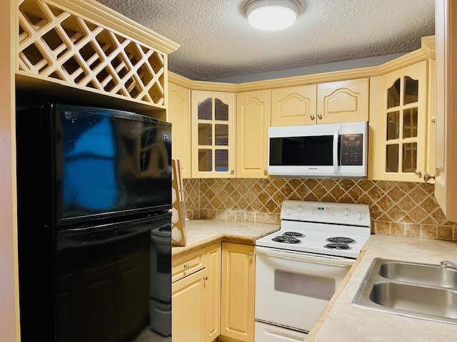 A kitchen features light-colored cabinets, a black refrigerator, a white stove, and tiled countertops — 4491 NW 1st Terrace, Deerfield Beach FL 33064, DEERFIELD BEACH, FL