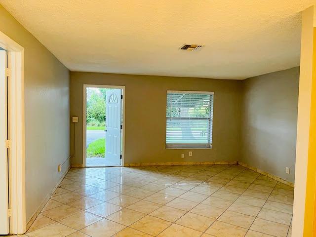 An empty room with light-colored tile flooring, gray walls, and an open exterior door — 4491 NW 1st Terrace, Deerfield Beach FL 33064, DEERFIELD BEACH, FL