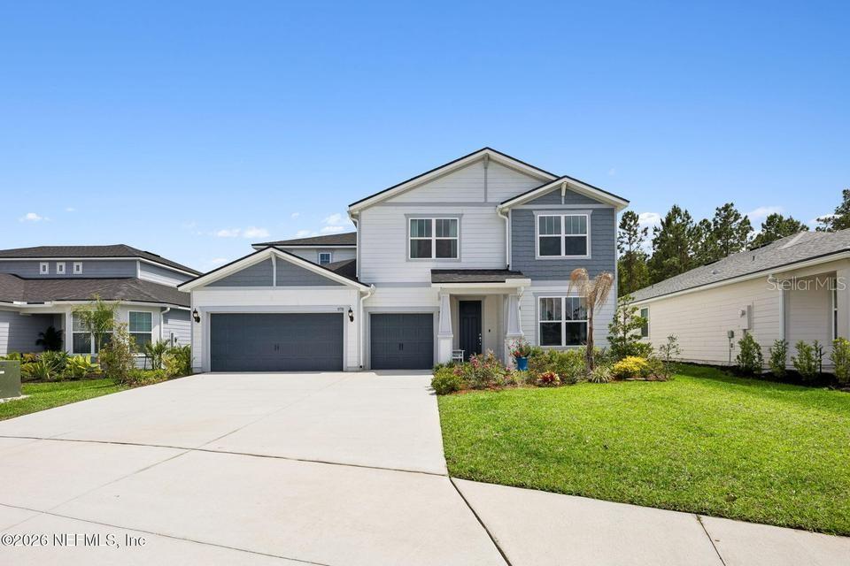 A two-story house with a three-car garage and light-colored siding sits under a blue sky — 978 ROOSTER HOLLOW WAY, MIDDLEBURG, FL