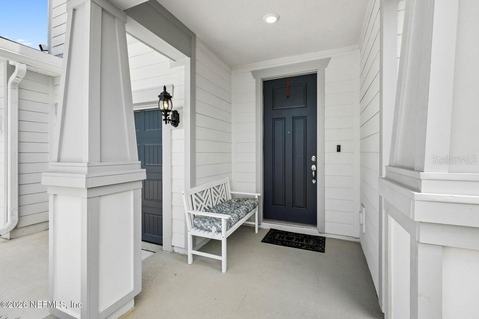 A covered front porch features a dark blue door, white siding, and a wooden bench — 978 ROOSTER HOLLOW WAY, MIDDLEBURG, FL