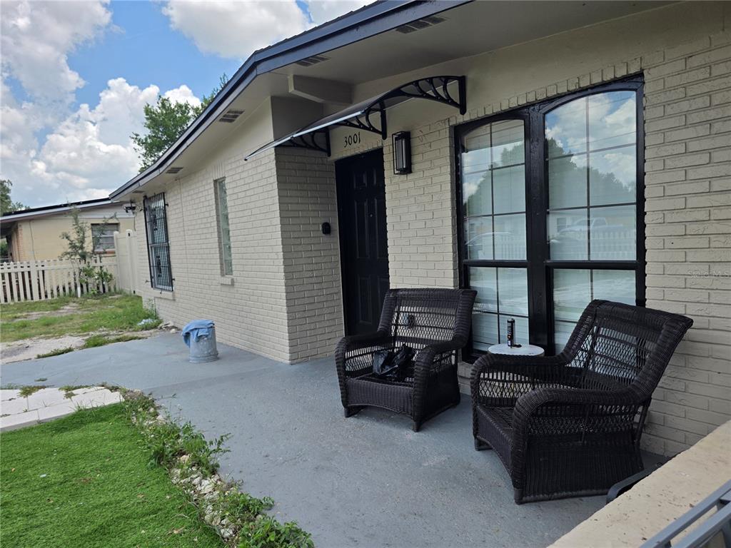A beige brick house exterior features a front porch with two wicker chairs and black trim — 3001 N 45TH STREET, TAMPA, FL