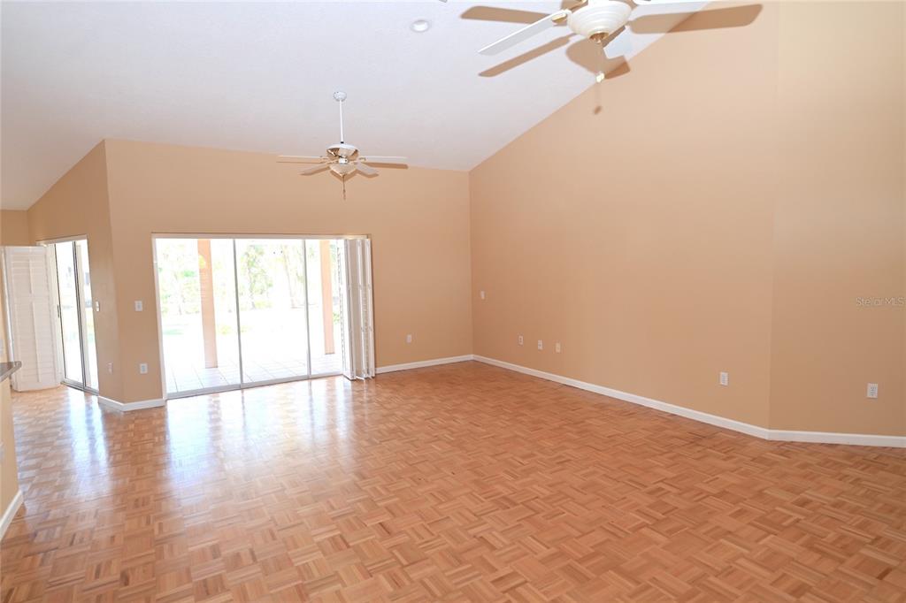 An empty living room features vaulted ceilings, parquet wood flooring, and sliding glass doors — 6535 CANARY STREET, SARASOTA, FL