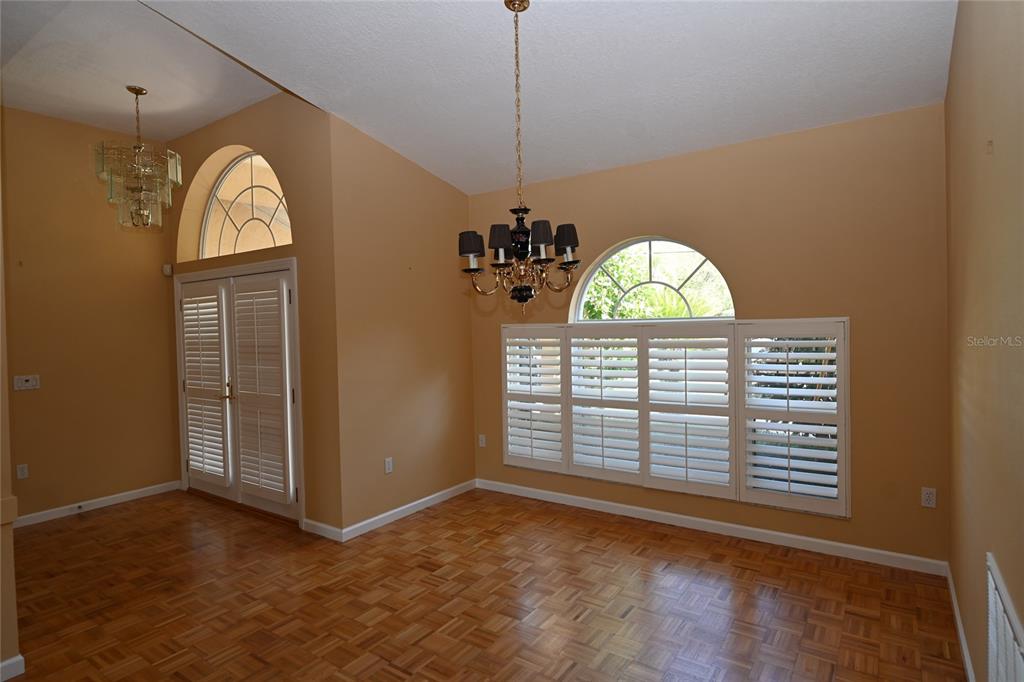 A dining room with hardwood parquet flooring, a chandelier, and arched windows with plantation shutters — 6535 CANARY STREET, SARASOTA, FL