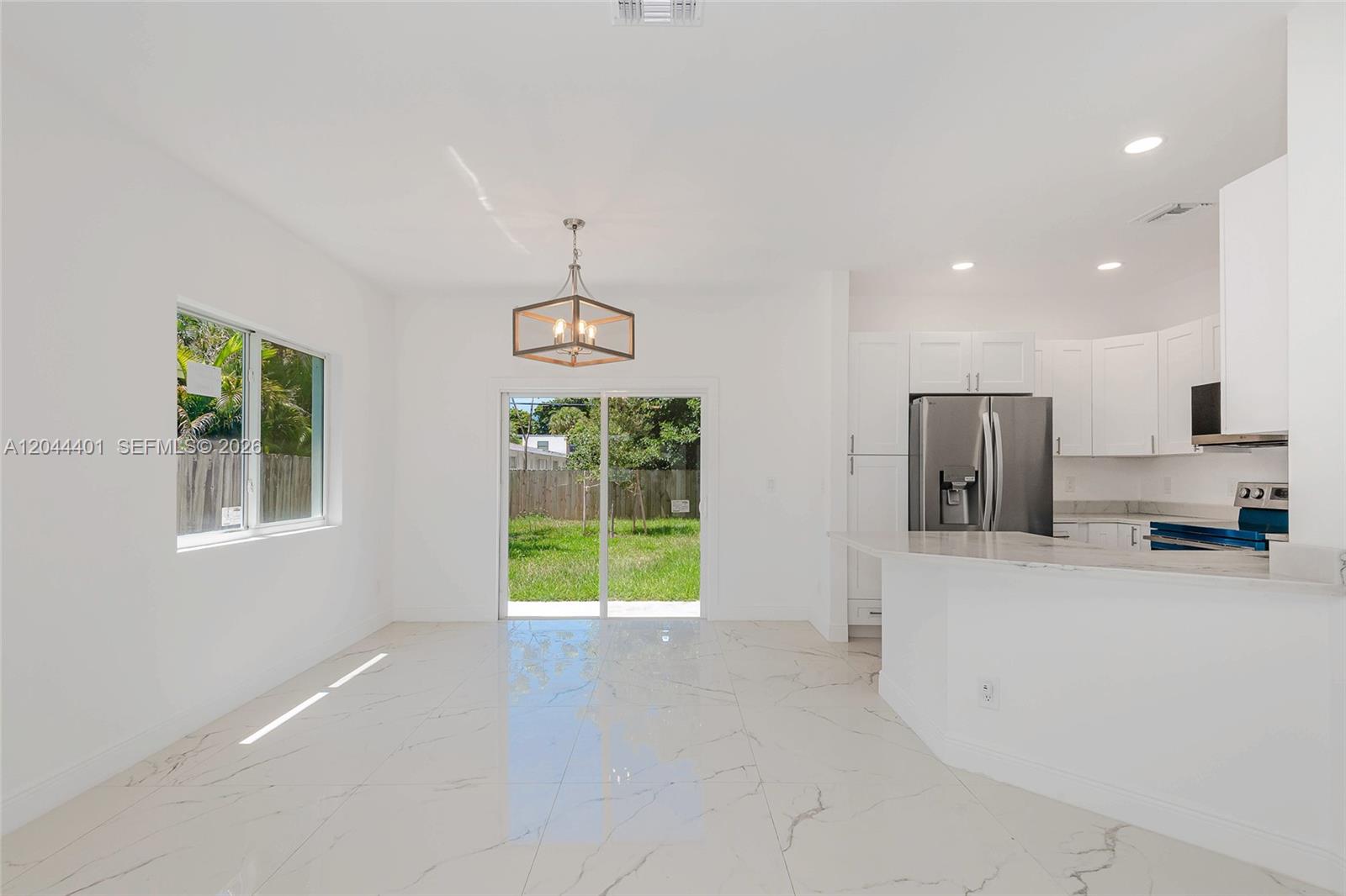 A bright dining area features white marble-look tile floors, a modern chandelier, and sliding doors — 731 SW 6th St, Dania Beach FL 33004, DANIA BEACH, FL