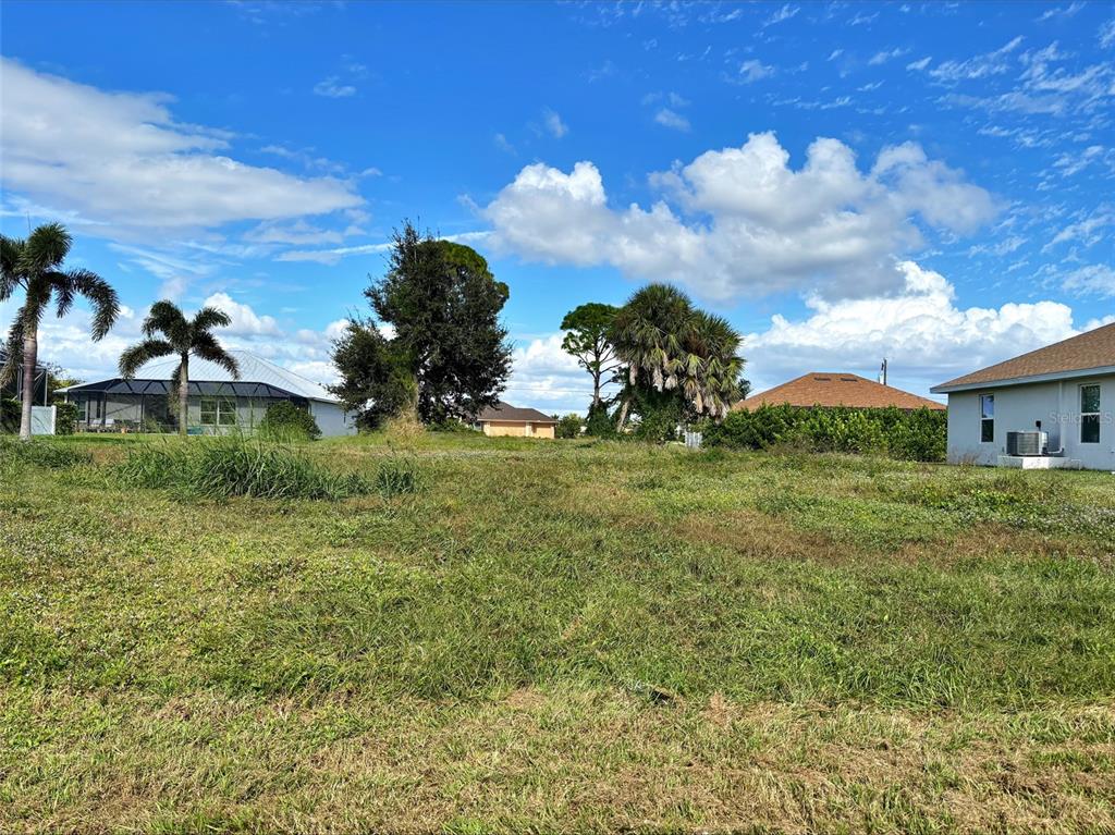 A vacant, grassy residential lot is surrounded by neighboring houses and various palm trees — 57 PINE VALLEY LANE, ROTONDA WEST, FL