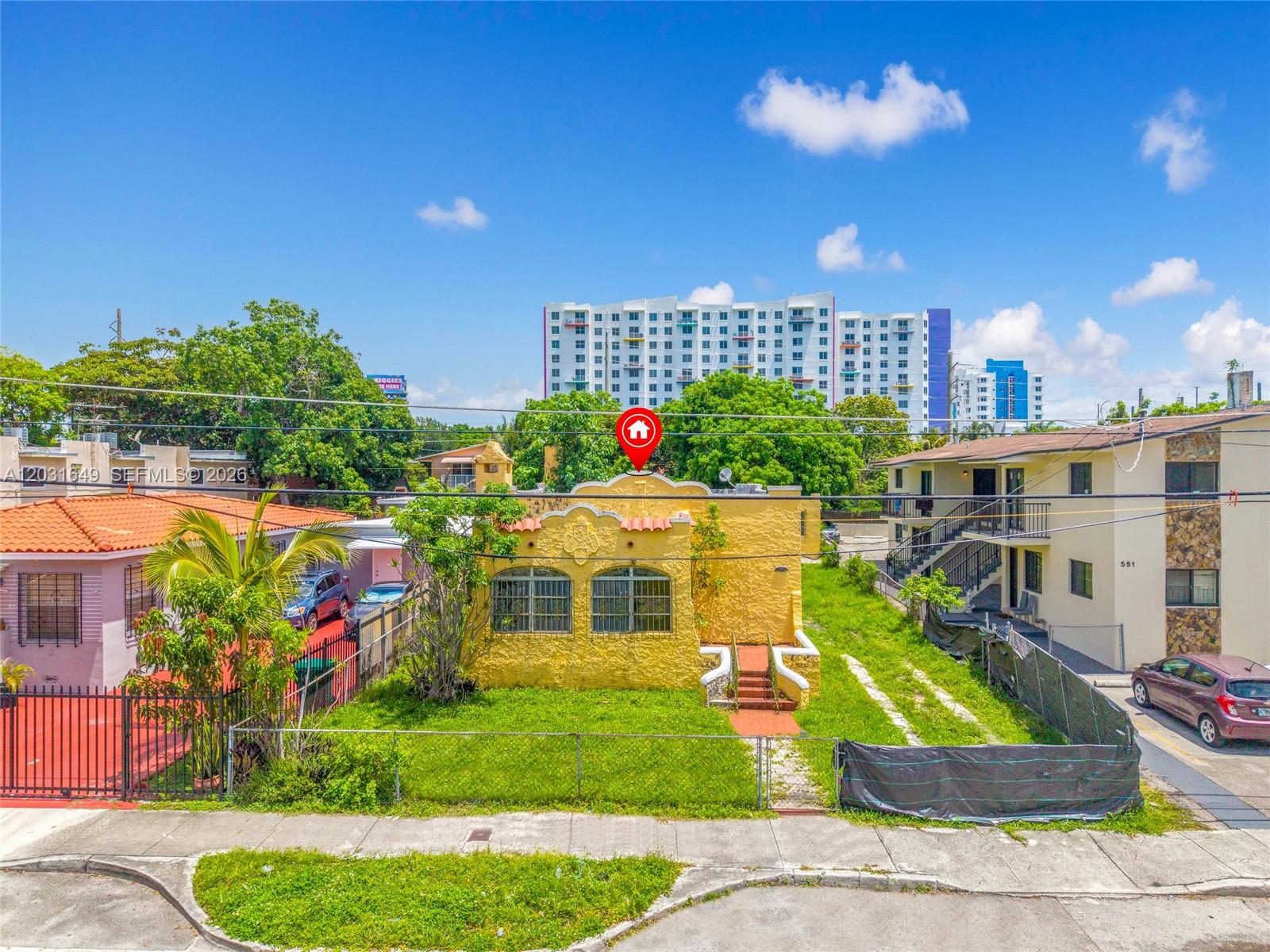 A yellow single-story house with a decorative roofline sits between two other residential buildings — 559 NW 34th St, Miami FL 33127, MIAMI, FL