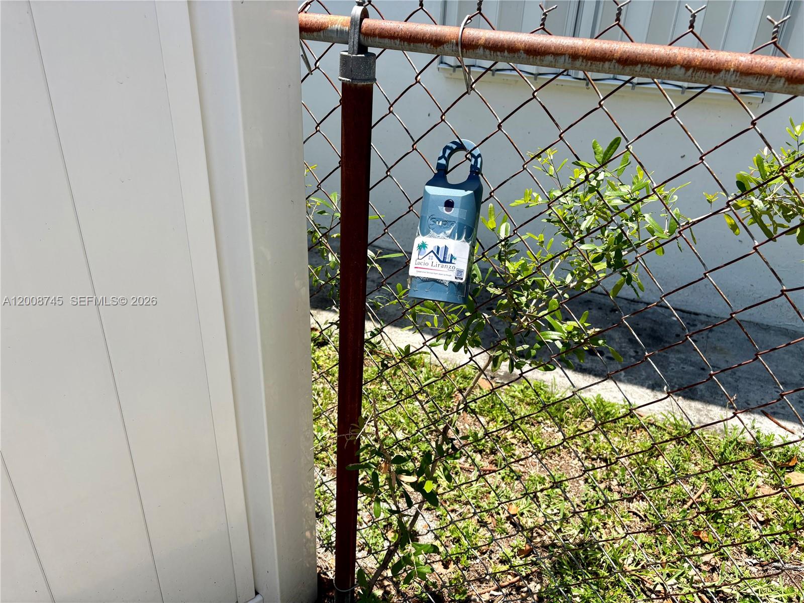 A blue Supra lockbox hangs on a chain-link fence next to a white wall — HOLLYWOOD, FL