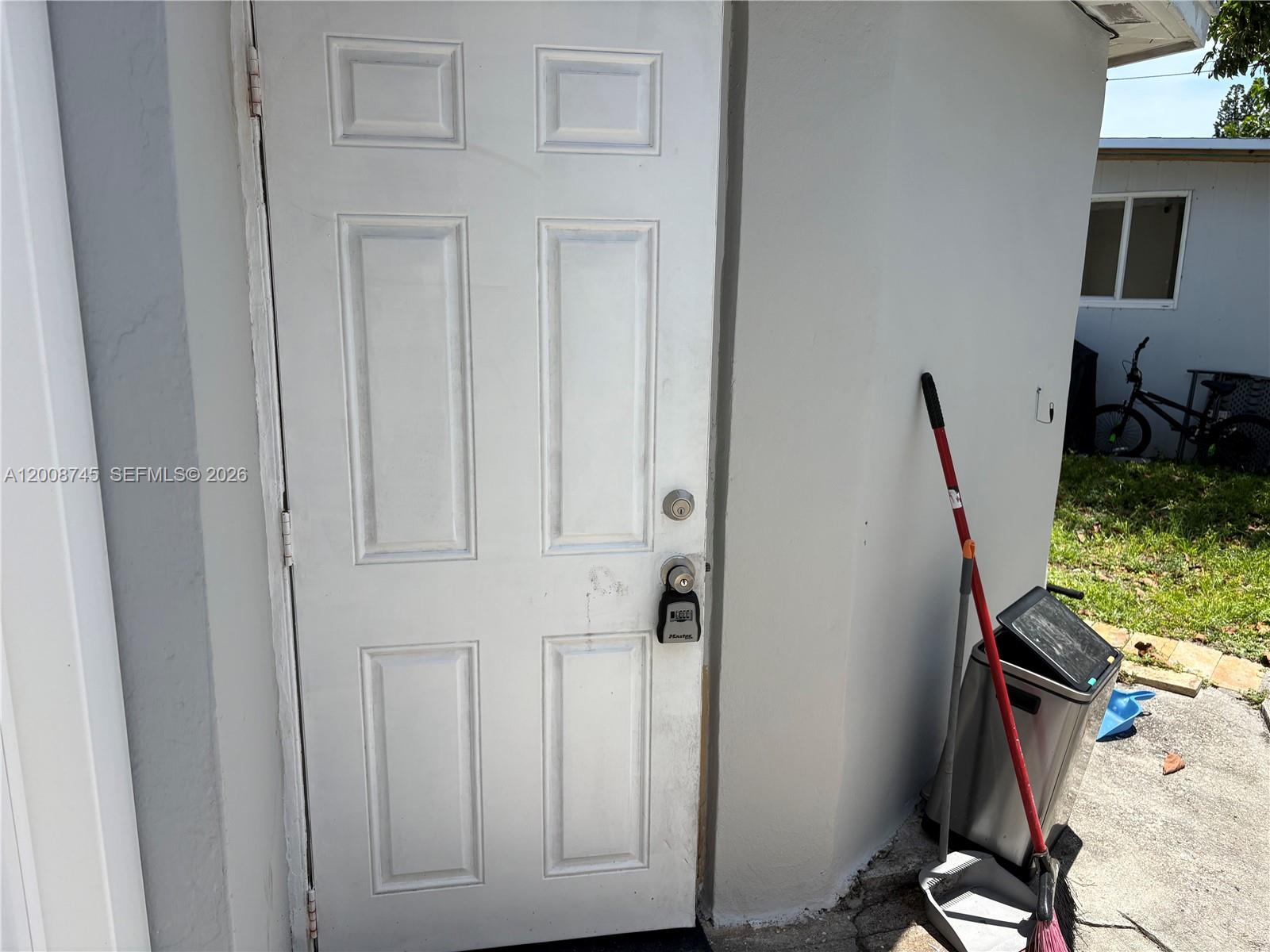 A white exterior door with a lockbox stands next to a broom and trash bin — HOLLYWOOD, FL