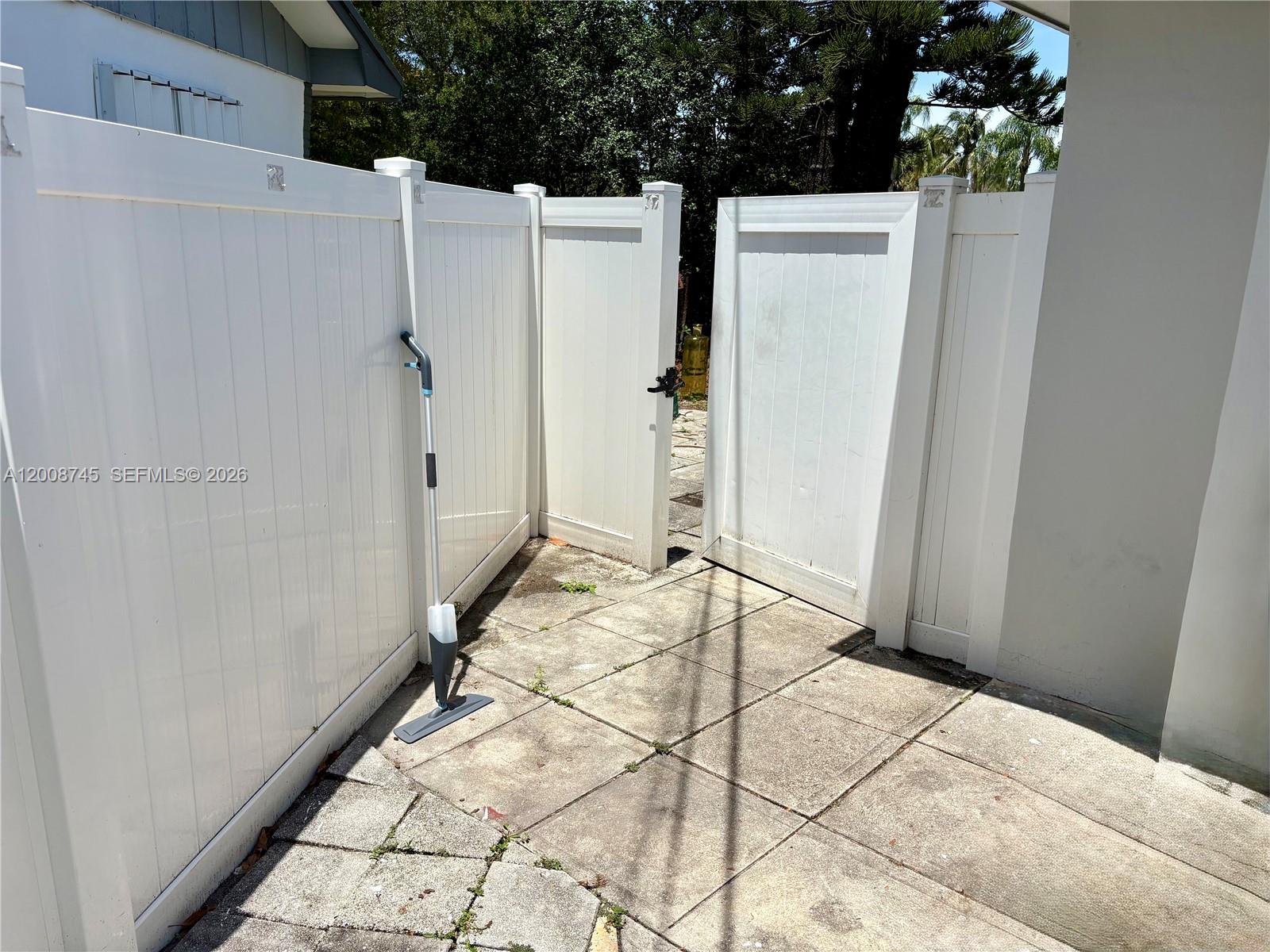A white vinyl fence with an open gate encloses a concrete patio area — HOLLYWOOD, FL