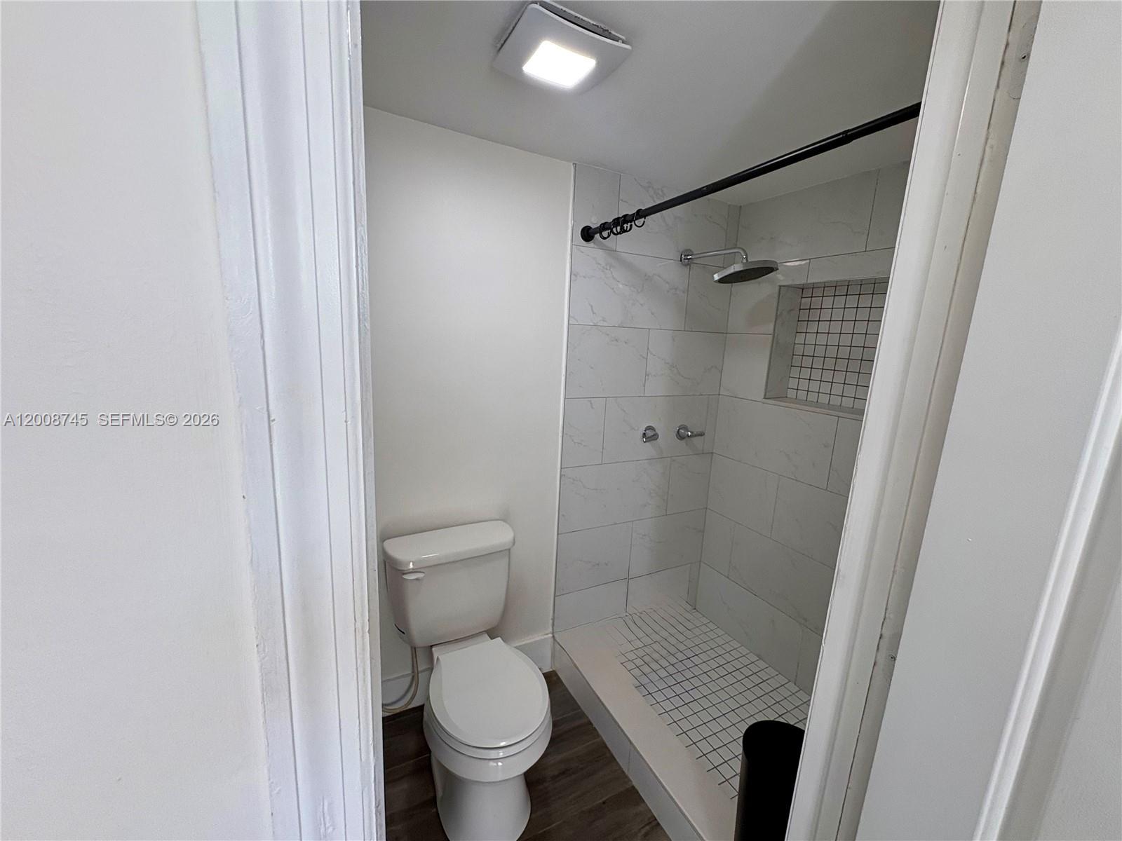 A small bathroom features a white toilet next to a tiled walk-in shower — HOLLYWOOD, FL