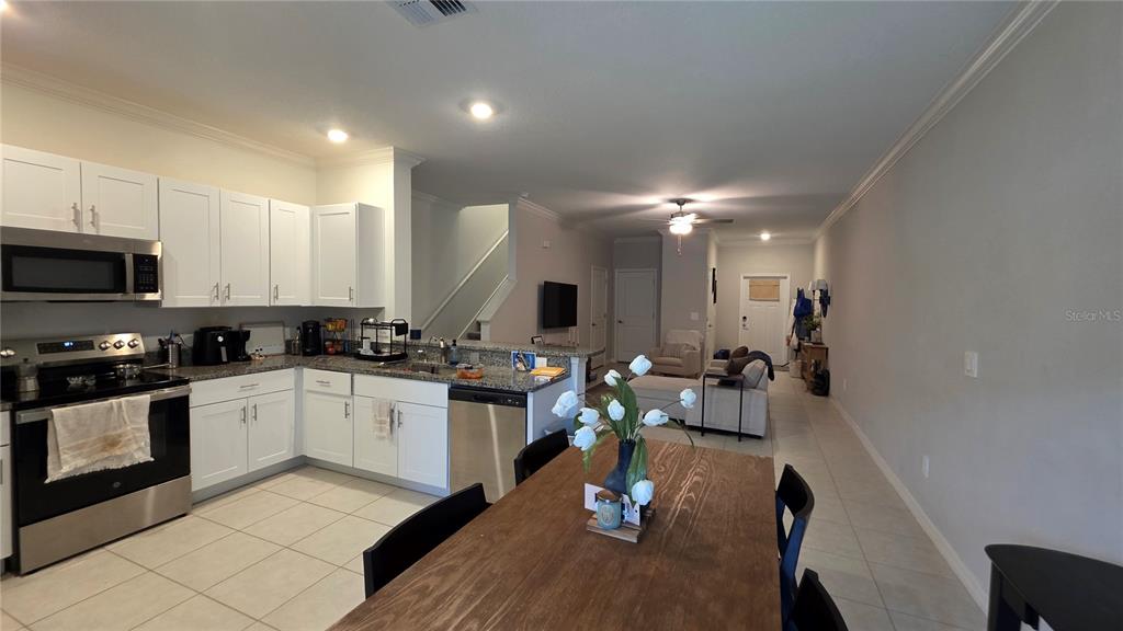 A kitchen with white cabinets and stainless steel appliances opens to a dining and living area — 36352 WELL HILL WAY, ZEPHYRHILLS, FL
