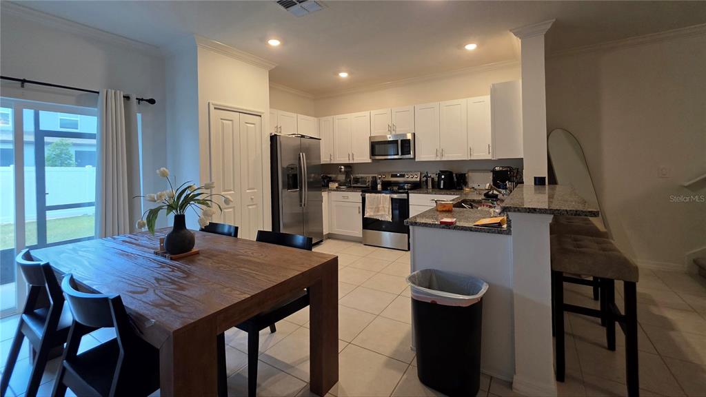 A kitchen with white cabinets and stainless steel appliances opens to a dining area — 36352 WELL HILL WAY, ZEPHYRHILLS, FL