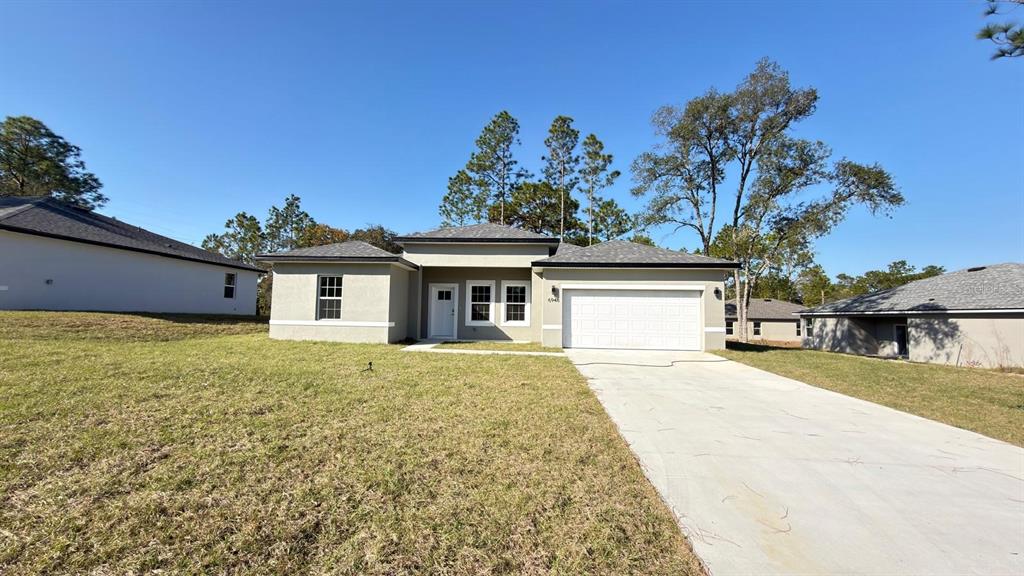 A single-story house with a beige stucco exterior, a two-car garage, and a concrete driveway — 6948 N ELKCAM BOULEVARD, CITRUS SPRINGS, FL
