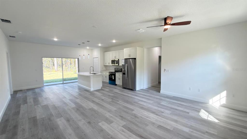 An open-concept kitchen and living area features white cabinetry, stainless appliances, and light wood flooring — 6948 N ELKCAM BOULEVARD, CITRUS SPRINGS, FL