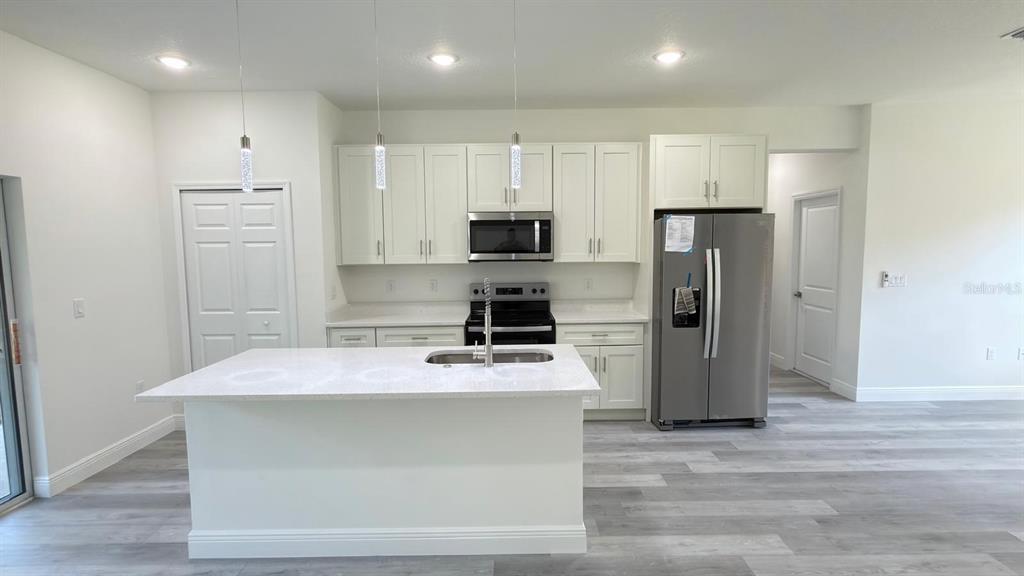 A kitchen features white cabinets, stainless steel appliances, a center island, and light wood flooring — 6948 N ELKCAM BOULEVARD, CITRUS SPRINGS, FL