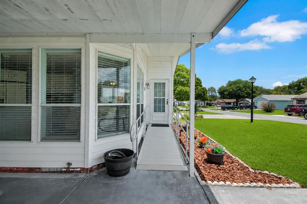 A white mobile home exterior features a wheelchair ramp leading to a glass-paneled entry door — 1203 GRANADA COURT, THE VILLAGES, FL