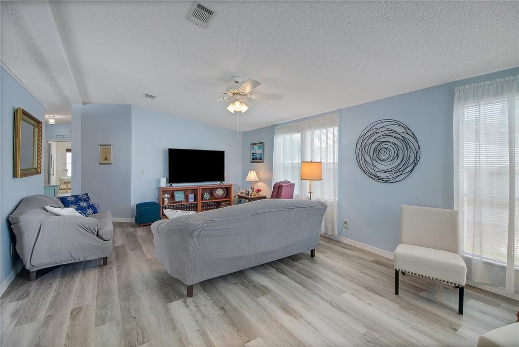 A living room features light blue walls, wood-look flooring, a ceiling fan, and neutral furniture — 1203 GRANADA COURT, THE VILLAGES, FL