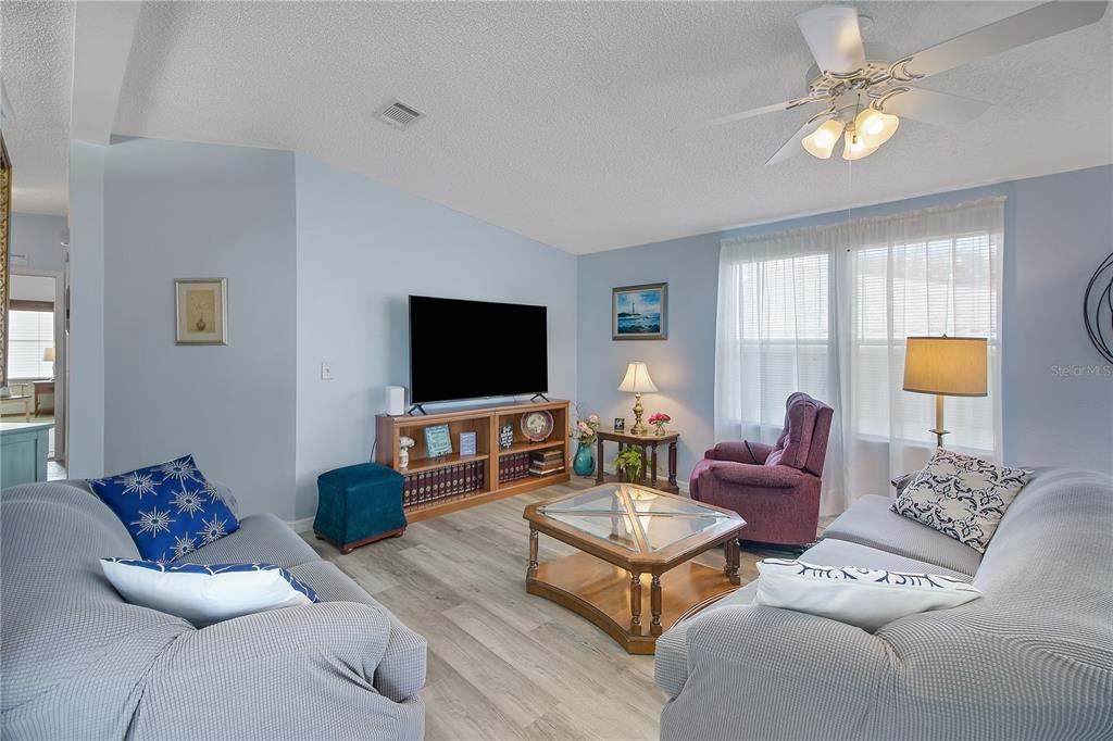 A living room features light blue walls, wood-look flooring, two gray sofas, and a television — 1203 GRANADA COURT, THE VILLAGES, FL