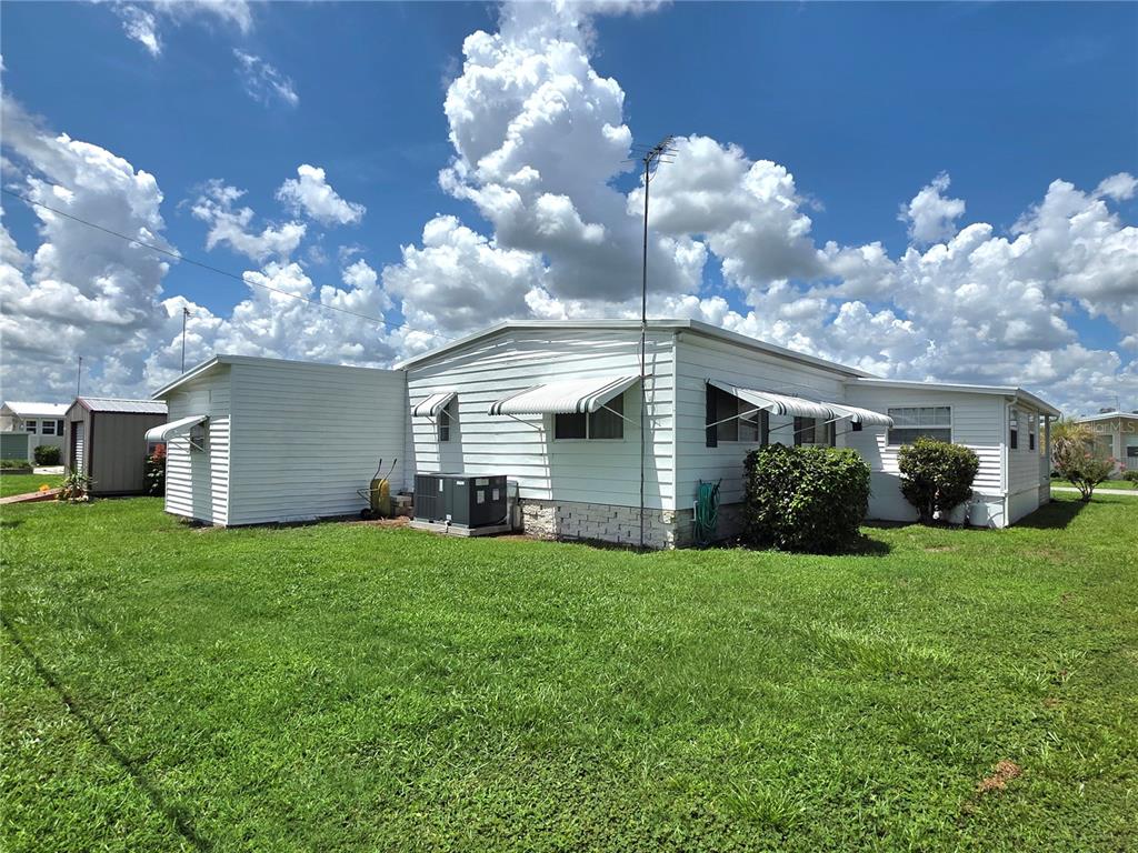 A white mobile home with metal awnings sits on a grassy lot under a cloudy sky — 5452 JOYCE STREET, ZEPHYRHILLS, FL