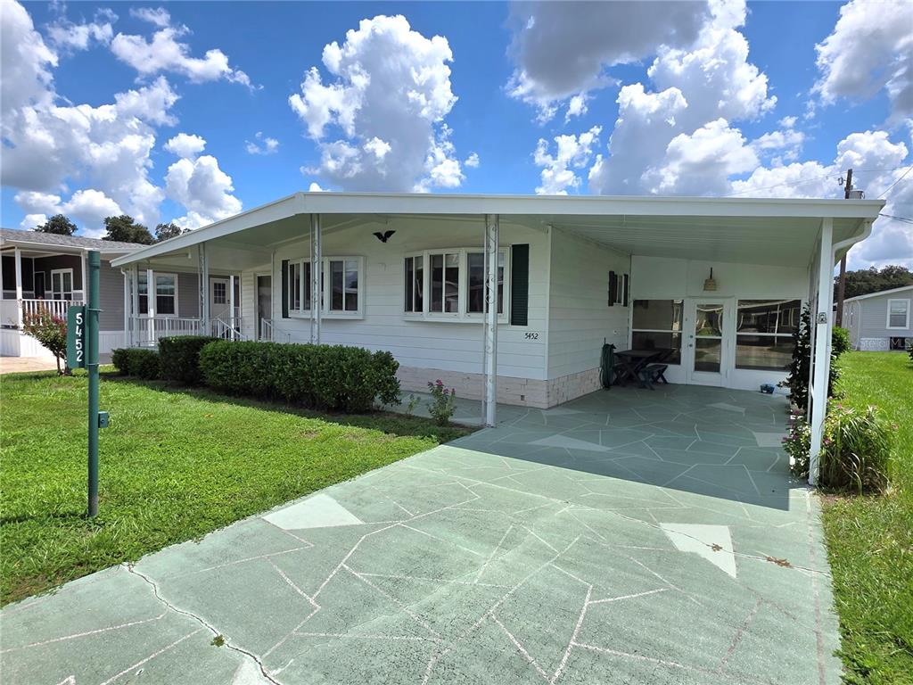 A white manufactured home features a green painted driveway and a covered carport — 5452 JOYCE STREET, ZEPHYRHILLS, FL