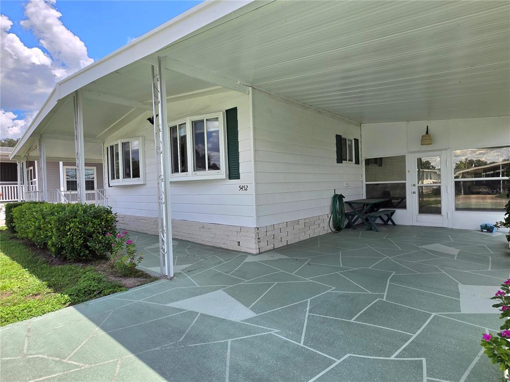 A white mobile home exterior features a large covered patio with a green patterned floor — 5452 JOYCE STREET, ZEPHYRHILLS, FL