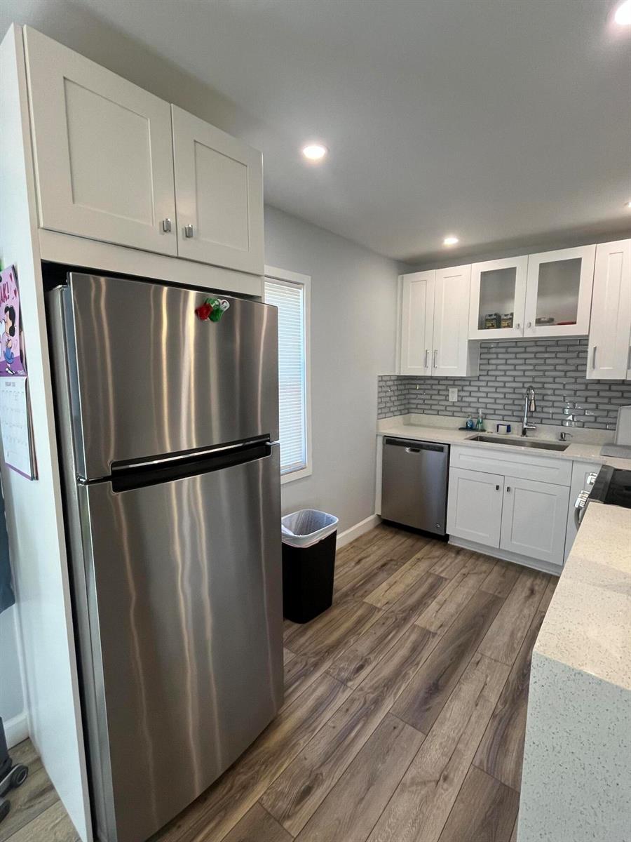 A kitchen features stainless steel appliances, white cabinetry, a gray subway tile backsplash, and wood-look flooring — 812 Burgundy Q, Delray Beach FL 33484, DELRAY BEACH, FL