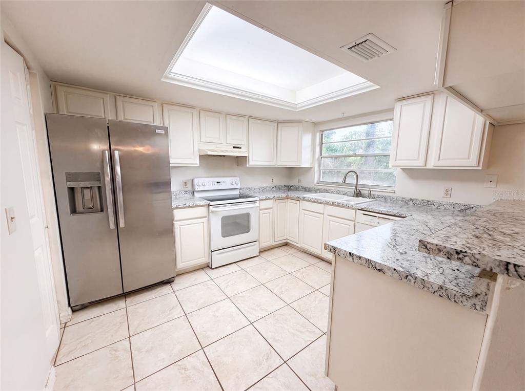 A kitchen features white cabinets, granite countertops, stainless steel appliances, and a large skylight — 4209 E ALENE DRIVE, TAMPA, FL