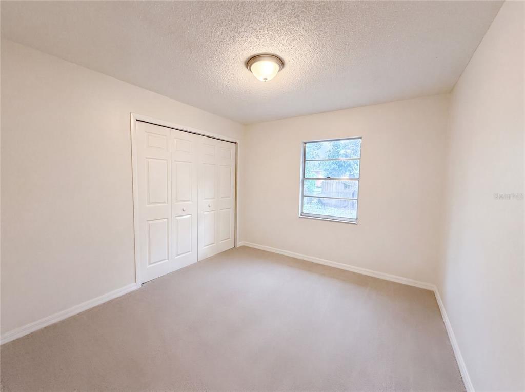 A bedroom features beige carpeting, off-white walls, a white bi-fold closet, and a single window — 4209 E ALENE DRIVE, TAMPA, FL